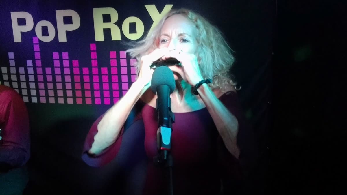 Toni René playing harmonica on stage in front of the Pop Rox backdrop